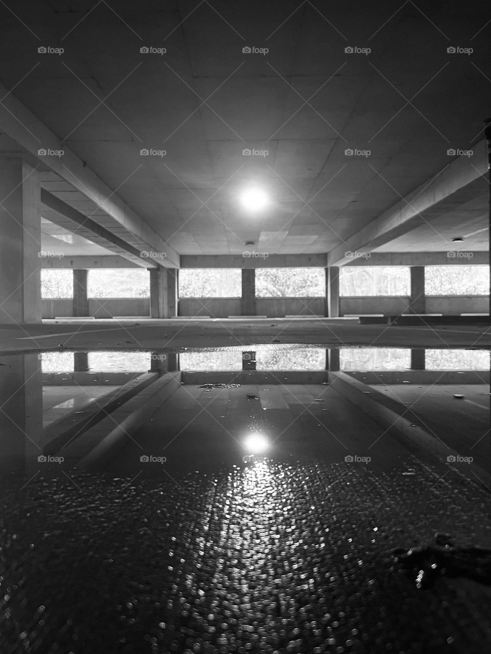 Concrete parking deck with puddle reflections in black and white. A desolate, eerie effect.