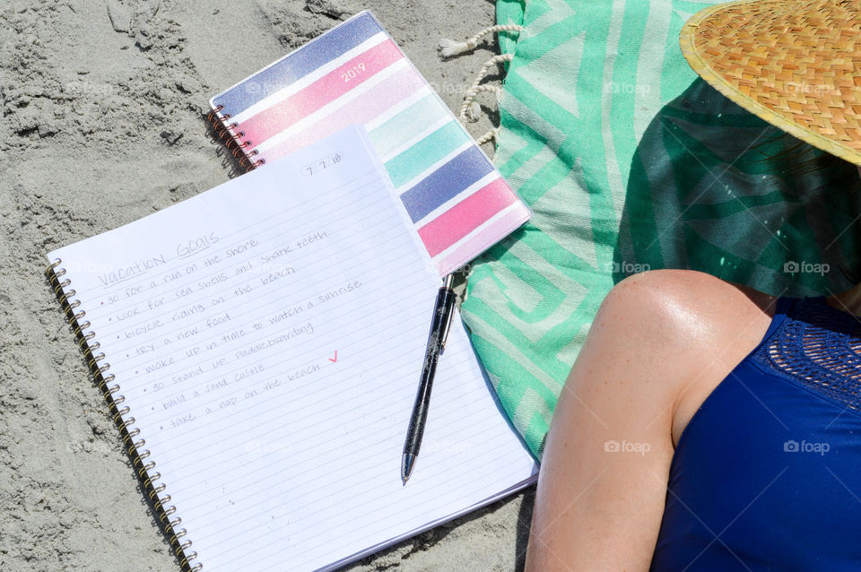 Notebook and planner laid out next to girl laying on the beach