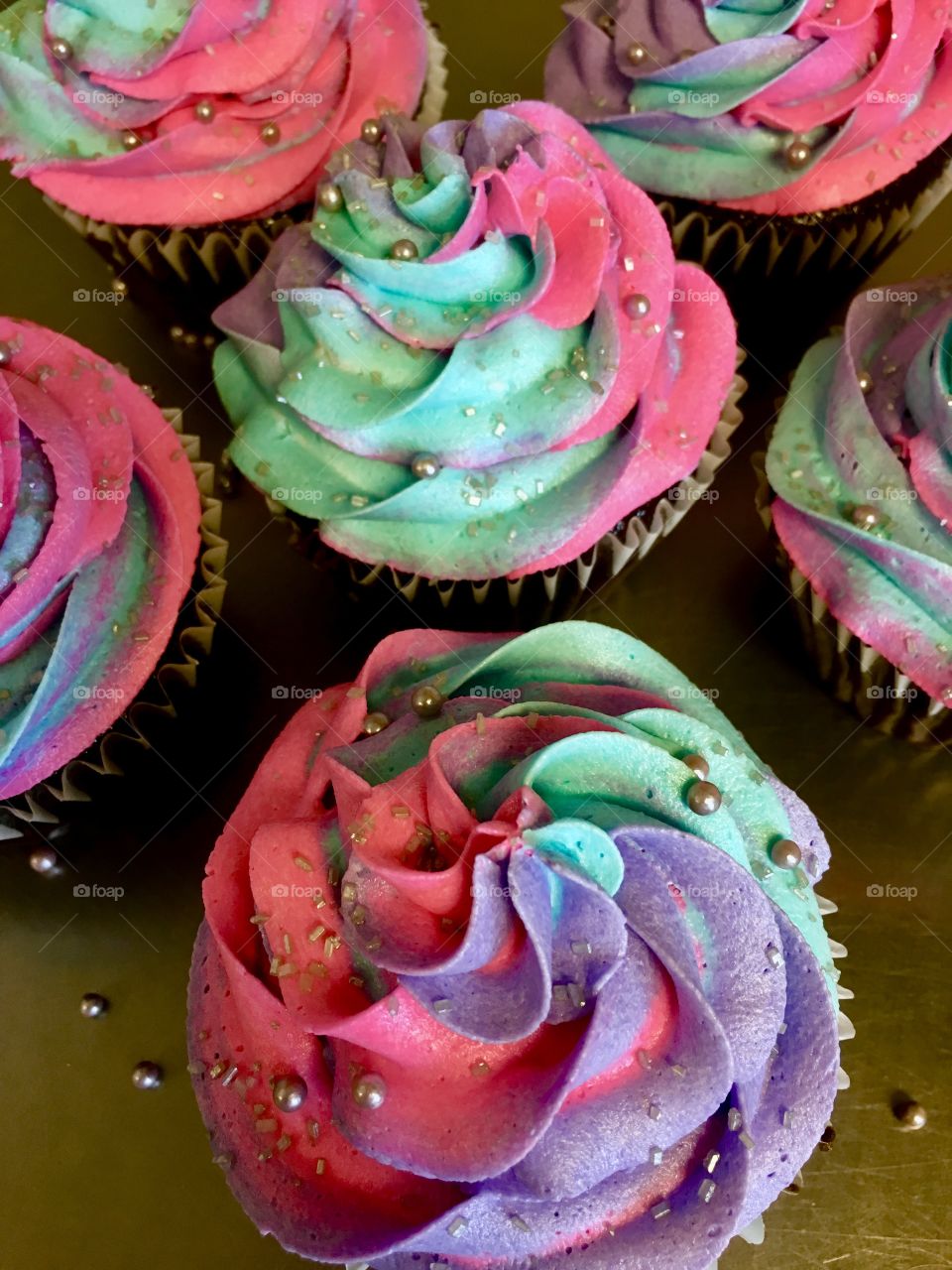 Pink, purple and turquoise swirled frosting on cupcakes with silver sprinkles.