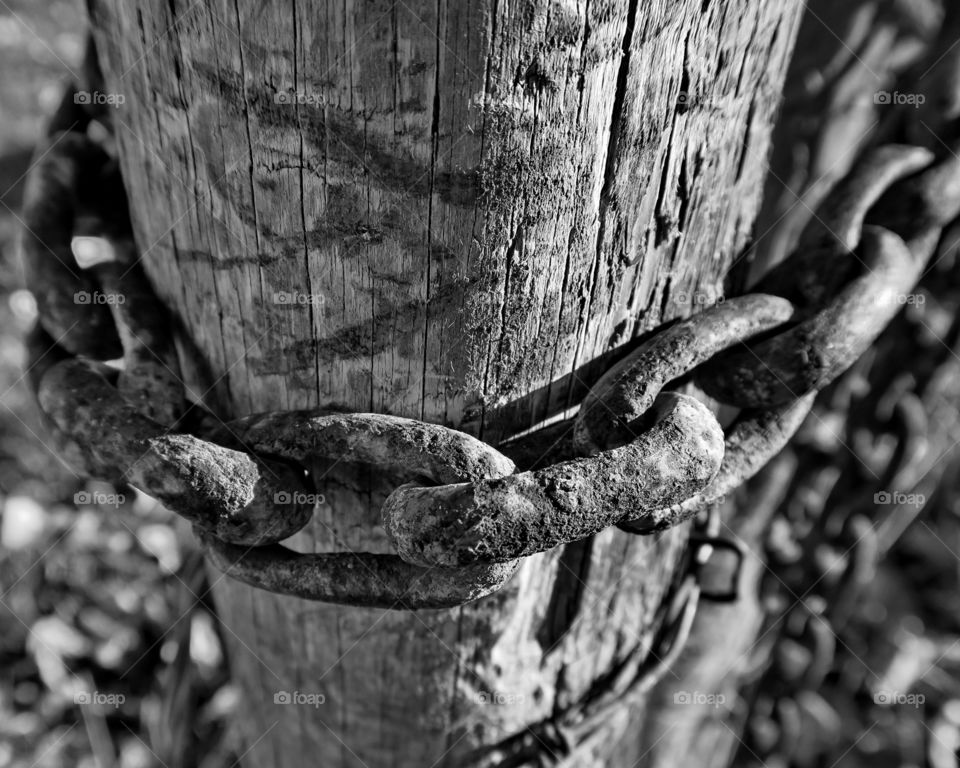 Rusty metal chain over old wooden post