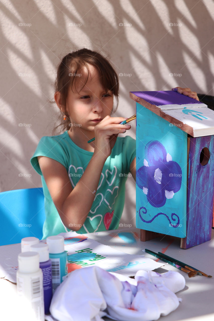 Child painting a wooden bird house