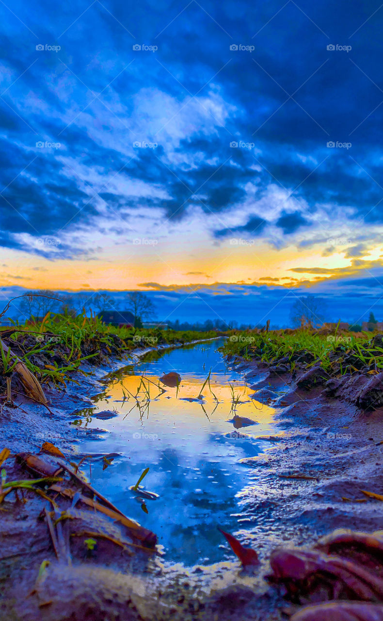 Dramatic and colorful sunset or sunrise sky reflected in the water of a puddle in a farmfield