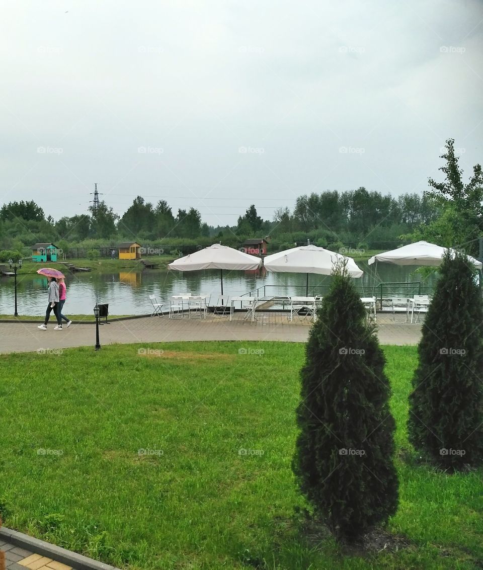 рукотворное озеро, пляжное кафе, пасмурно,люди под зонтиком, дождь,зелёные газоны серые облака