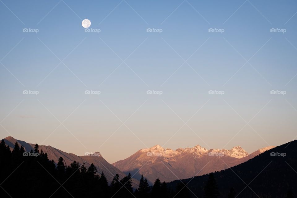 A moment of day greeting night , Moon over Caucasus Mountains in morning twilight time