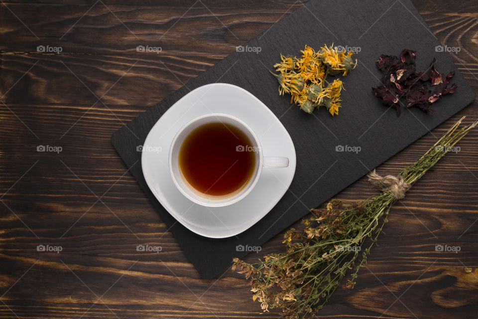 cup of herbal tea on slate board on a wood table. calendula and St. John's wort grass