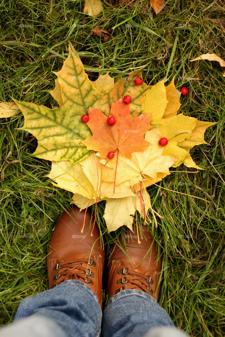 Selfie photo of feet in the autumn shoes with harvested maple leaves and hawthorn berries
