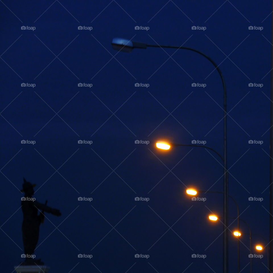 statue's silhouette directing  a  concert of lights street