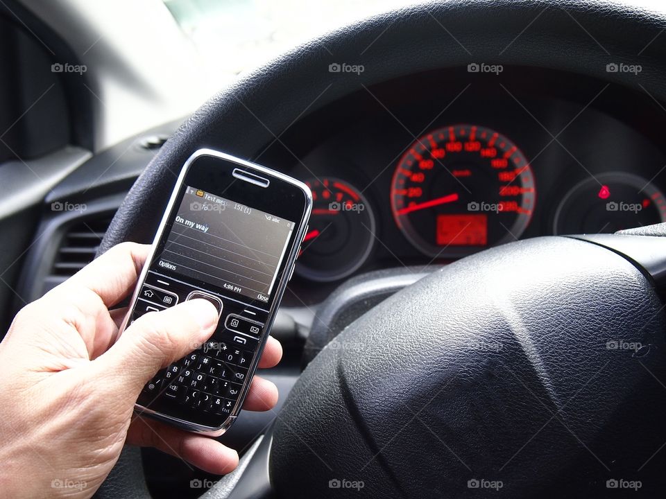 hand holding a cellphone in front of a car's steering wheel