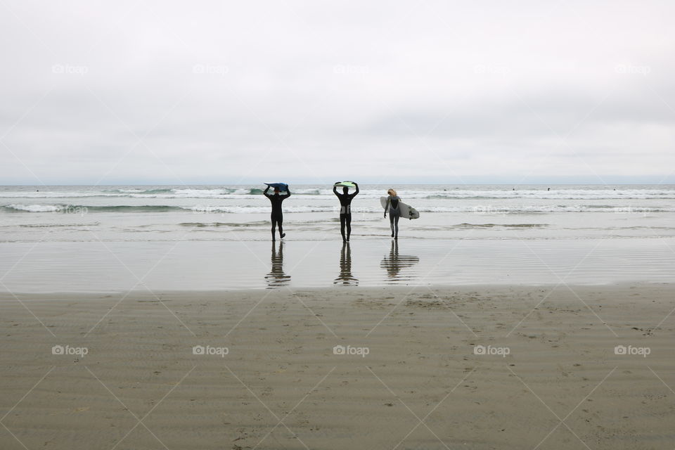 The waves are calling those enthusiastic people to come in the ocean .. their surfboards up on the head or arms , suited properly for the chilly weather , they are excited to ride on ... 