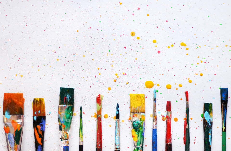 Artistic, colorful flat lay of paintbrushes and splash paint on white background