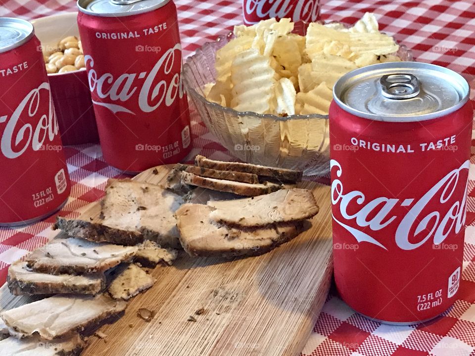 Cans of Coca-Cola on a red and white checkered background with barbecue food and potato chips 