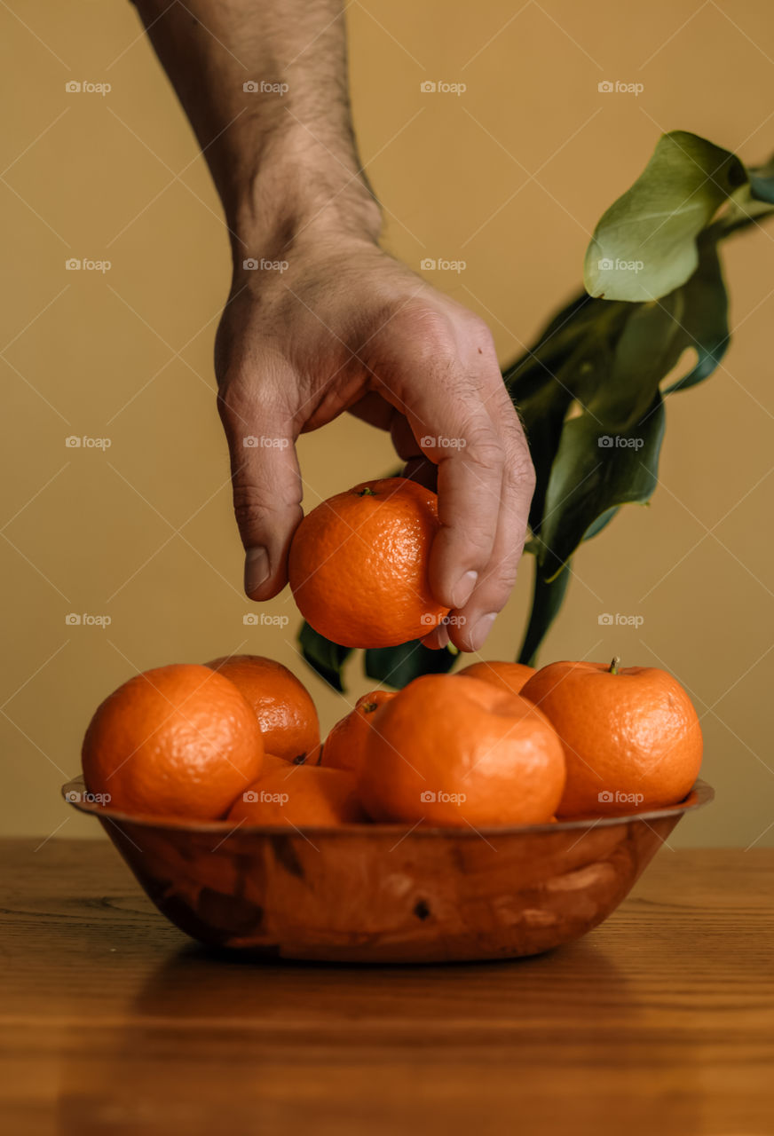 Cropped hand of man holding tangerine fruit on table.