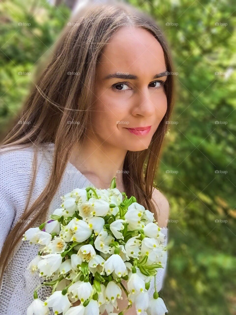 Portrait of dark blonde woman in the forest holding a snowdrops bouquet