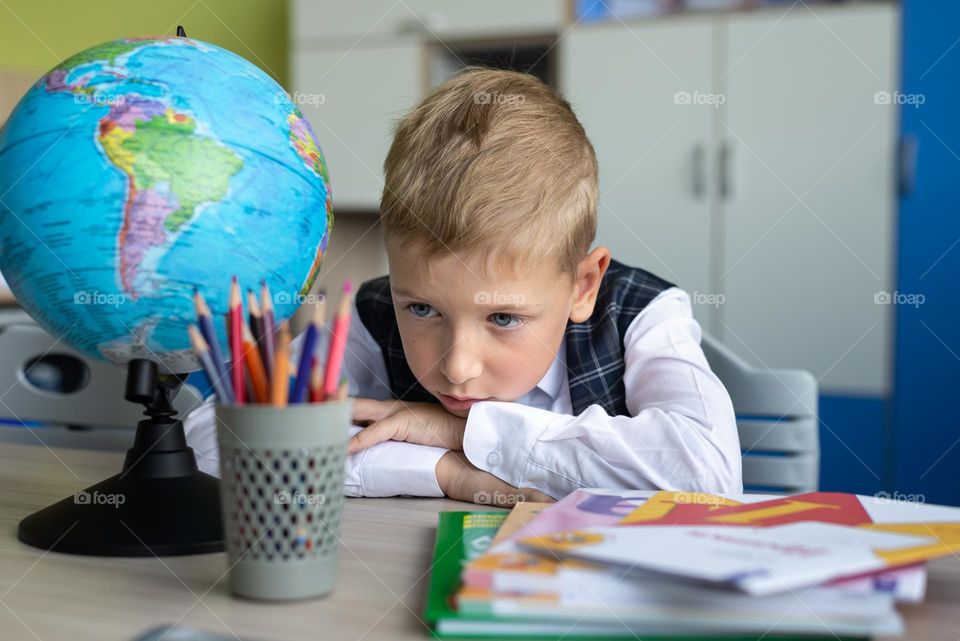 a first-grader child is sad at his desk at school, next to the globe