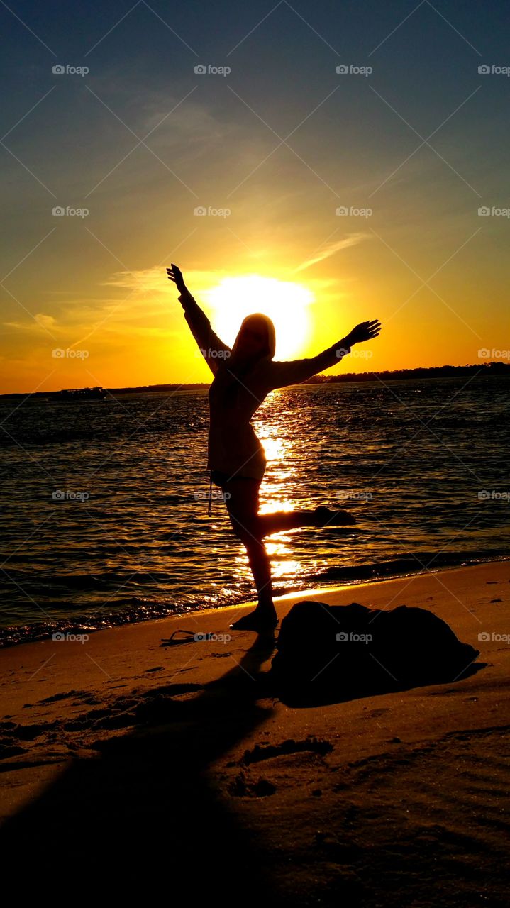 Silhouette of a woman dancing near the coast at sunset