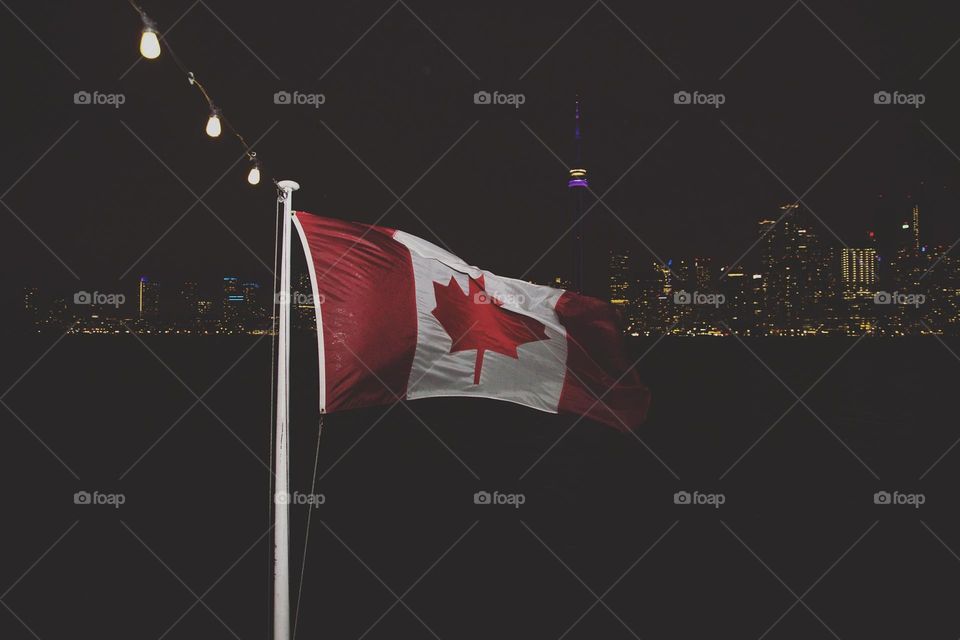 beautiful Canada flag waving in Lake breeze wind off of lank Ontario at night with Toronto skyline in background