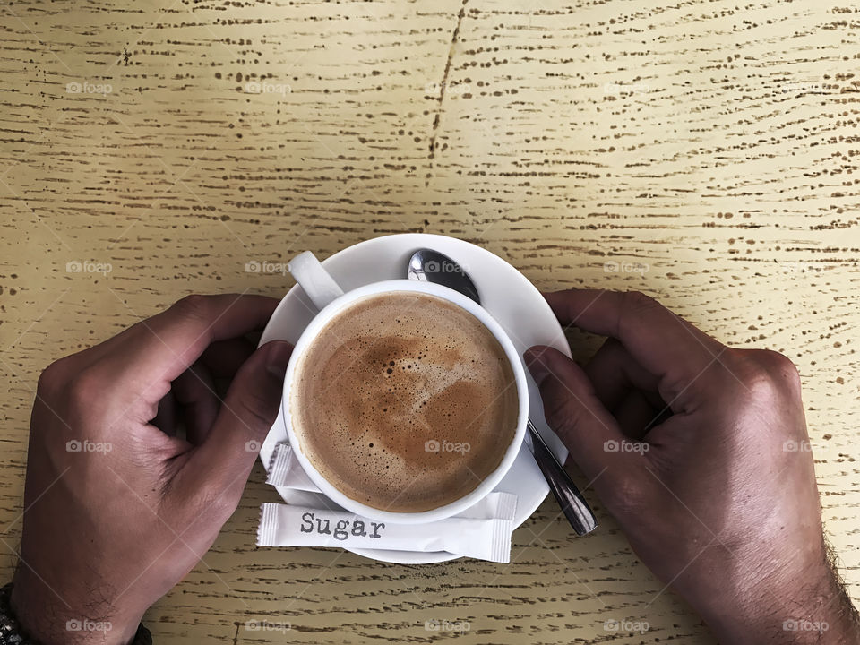 Overheard view of male hands holding favorite cappuccino on wooden table in the morning 