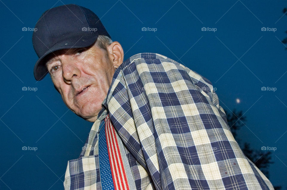 Elderly man with a baseball hat stands under a moonlit night