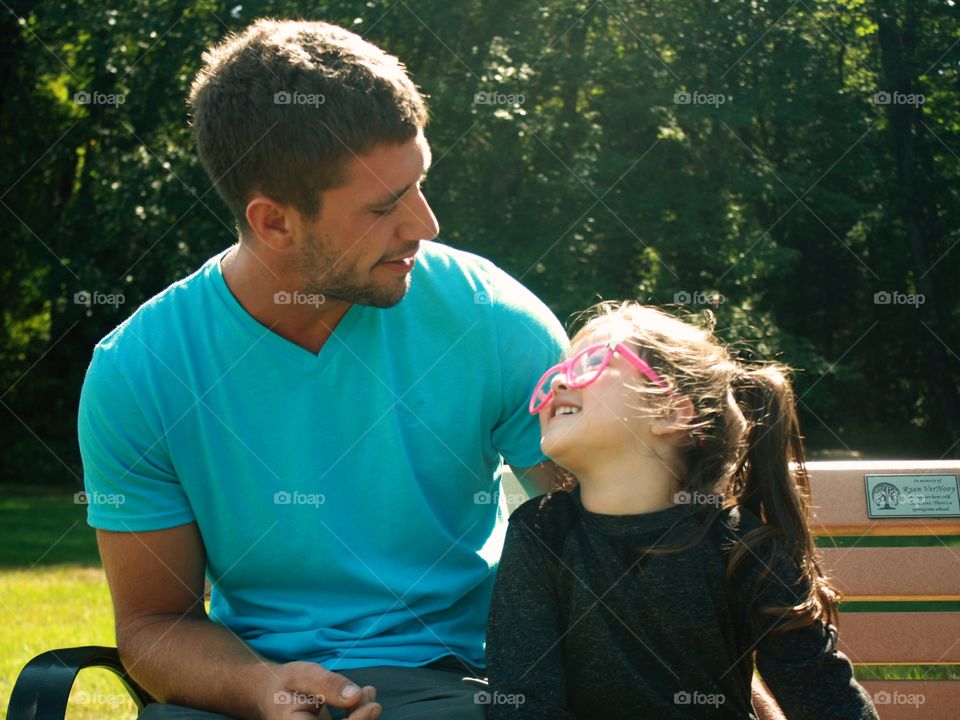 Father and daughter sitting on bench in park