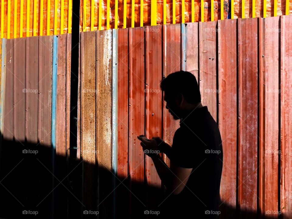 Silhouette of a man on the phone against bright metal deck wall