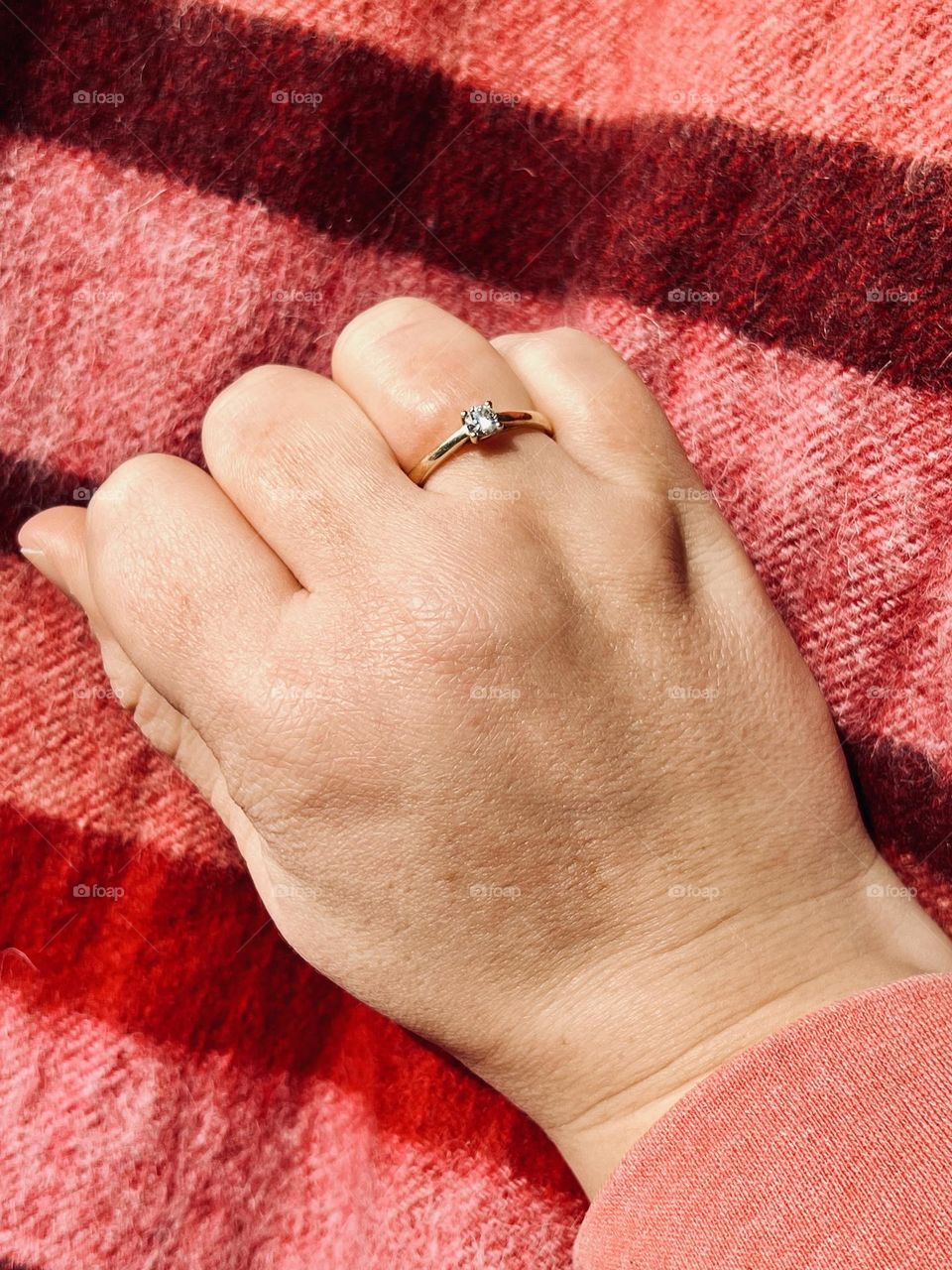 Female hand with engagement ring on a red cloth lying in the sun.