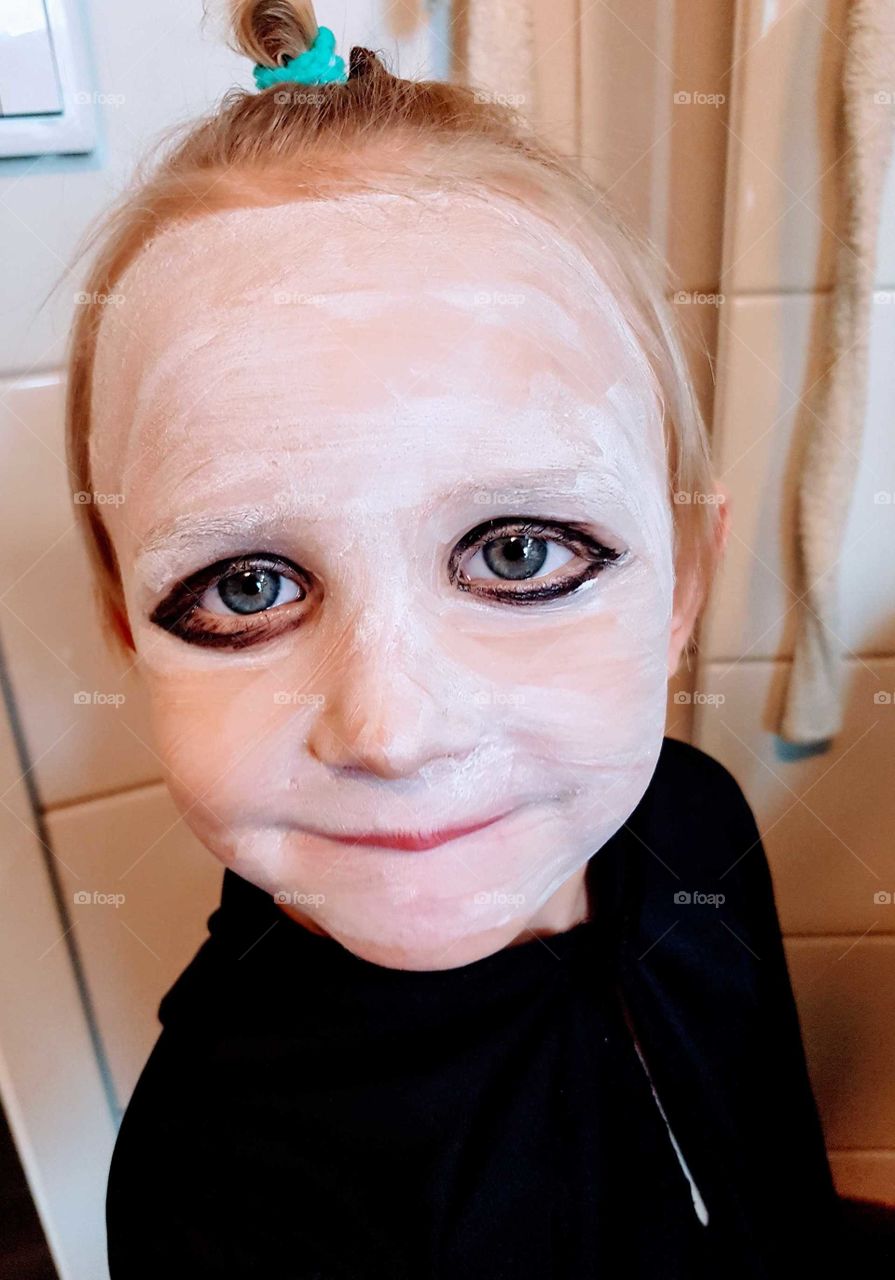 Little boy with big eyes putting in makeup for Halloween