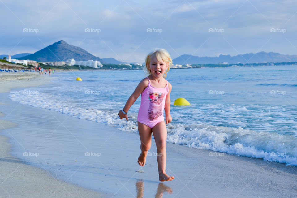 Happy little girl of four years old running on the beach in Alcudia on Majorca. Alcudia Pins Resort and hotel.