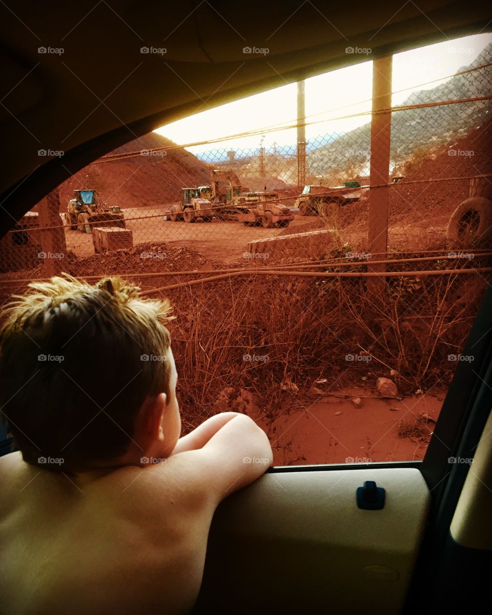 A kid is watching from car window a bauxite factory 