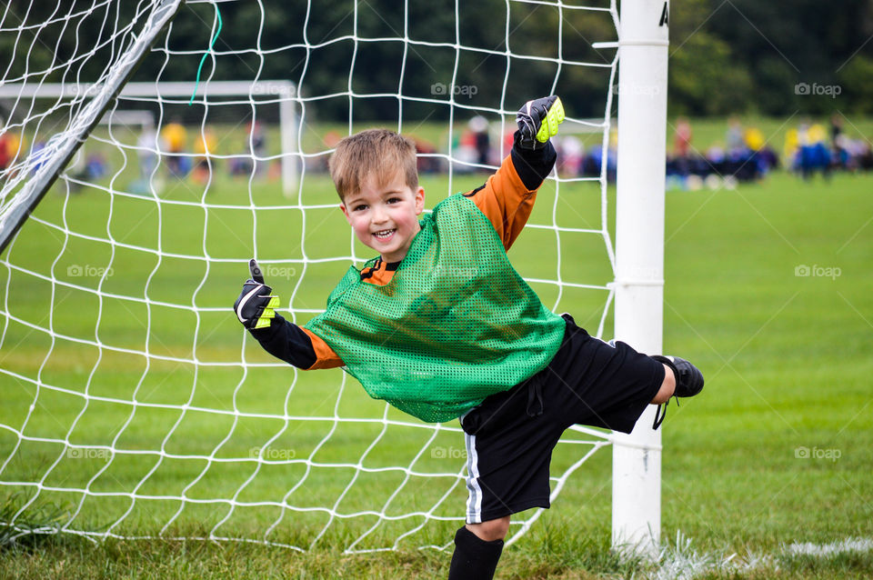 Young smiling boy playing goalie during a soccer game and giving thumbs up