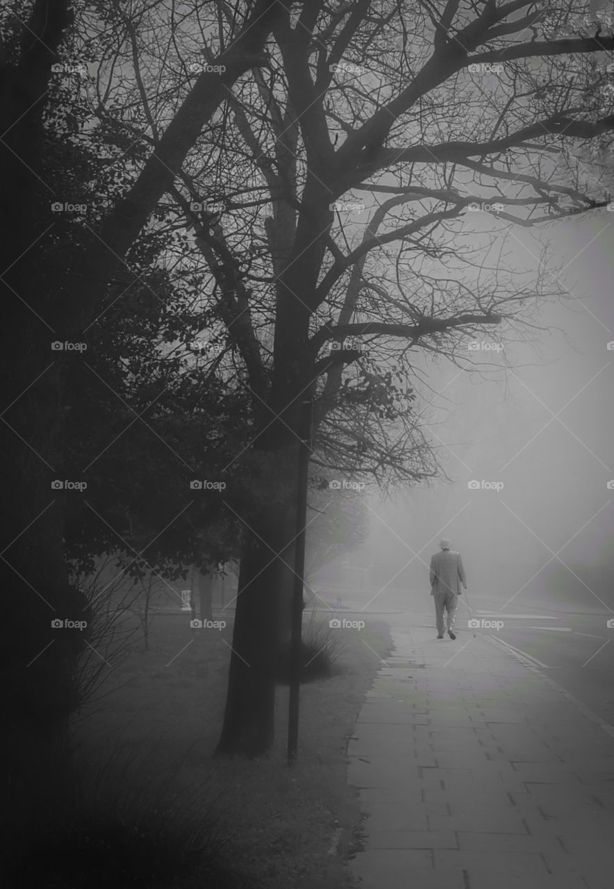 An old man walking away into the fog