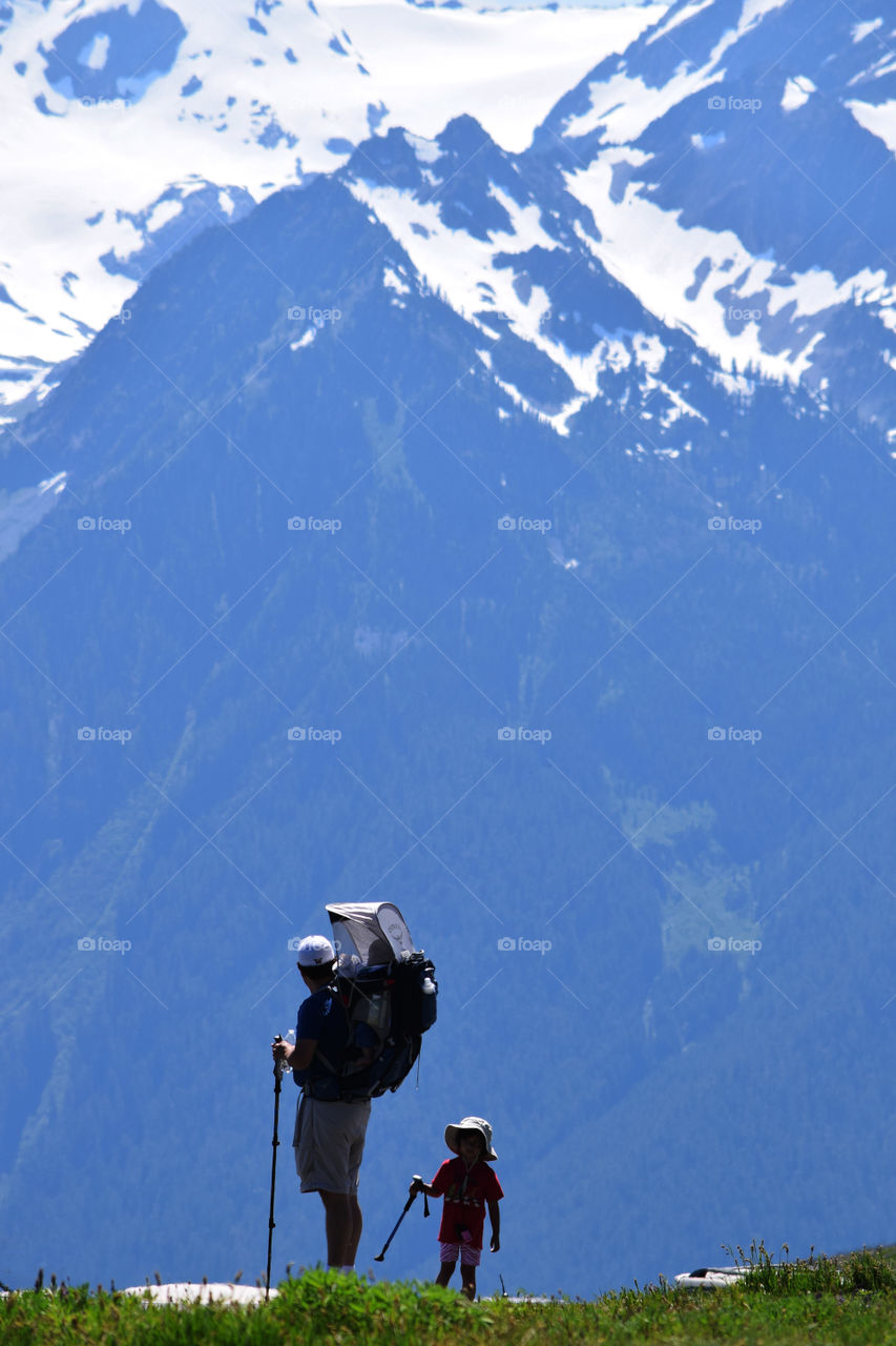 A father and his children's (baby on his back) silhouette against the mountains.