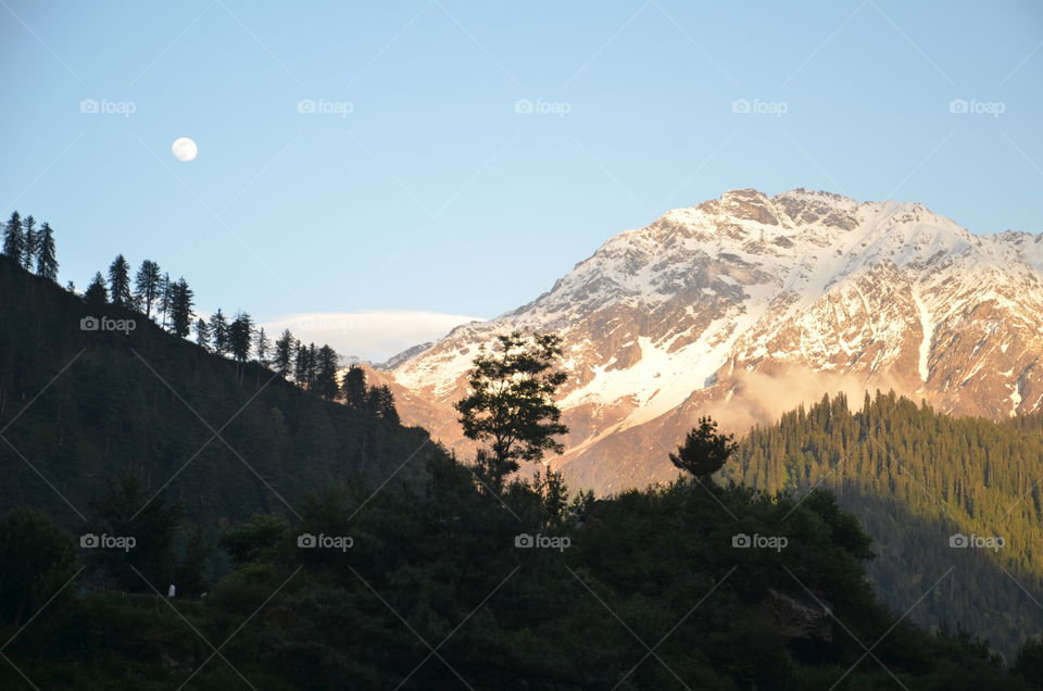 icy mountain with sunlight rays and moon light 
himachal beauty