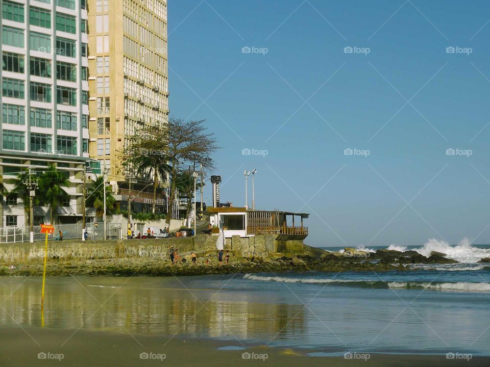 Pitangueiras Beach at Guarujá, Brasil. We see the shore, the rocks and the reflections of the sea and the skyscrapers.