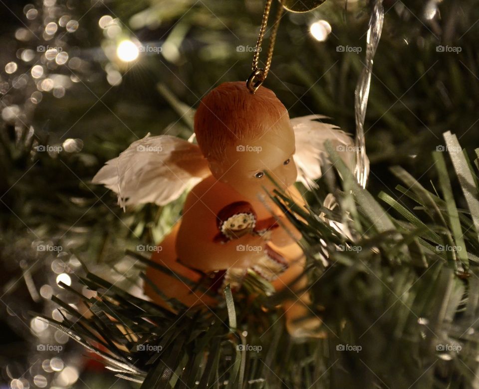 An ornament of a baby angel holding a gingerbread cookie hanging in a tree