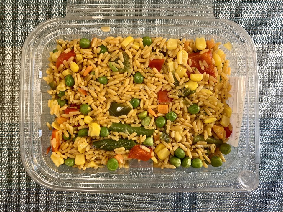 Rice and mix vegetables in a transparent container with sky blue background. Lunch and dinner. Take out. Open.