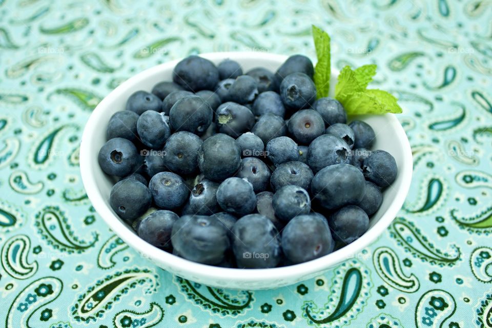 Fruits! - Blueberries and a spring of mint in a white bowl on teal and green paisley fabric