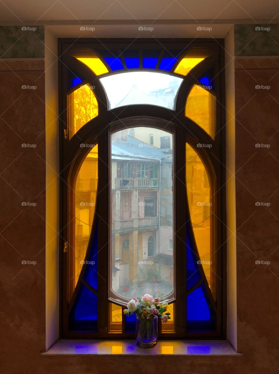 Flowers in a vase on a windowsill near a colored big window 