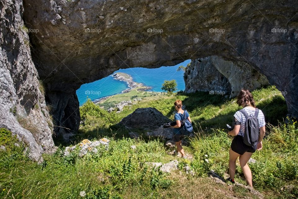 Two female hikers walk through a natural arch on top of a mountain 
