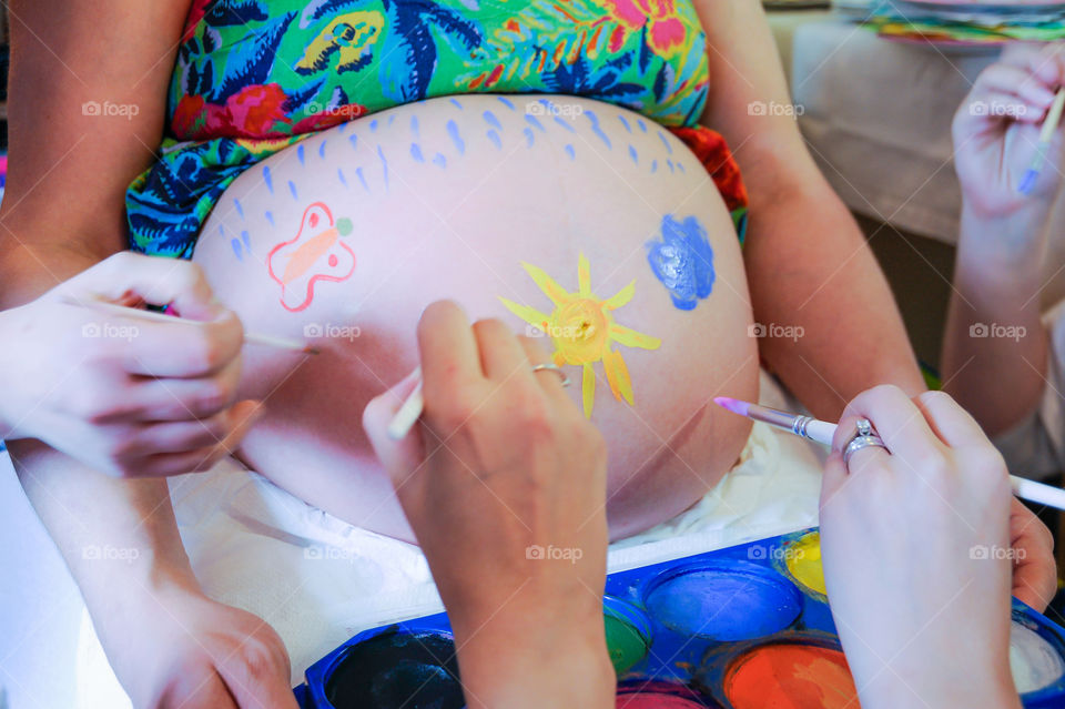 Beautiful pregnancy moment. Pregnant woman having her belly painted by her friends.