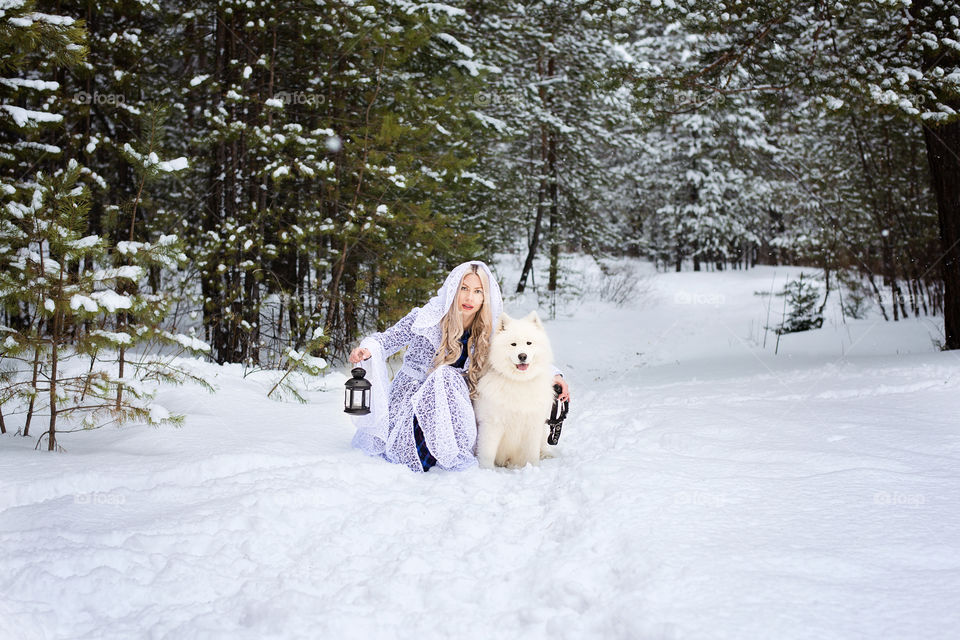 Young woman sitting with white dog in snow at winter