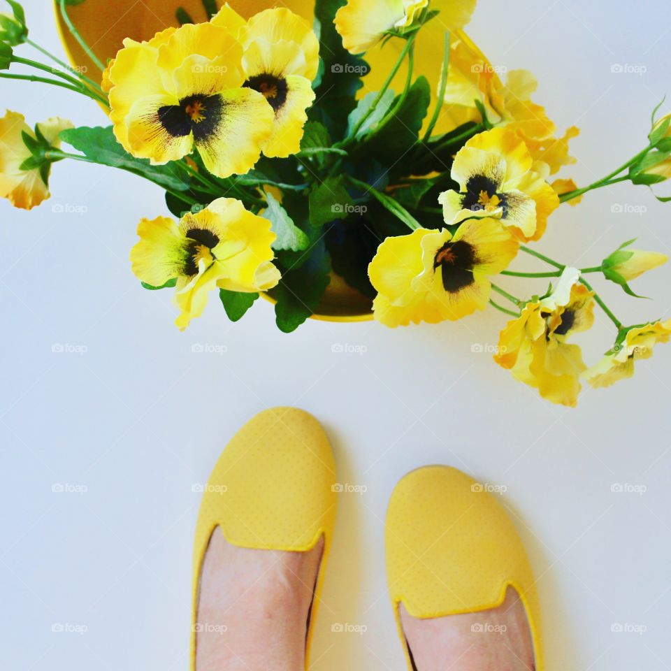Woman wearing yellow shoes stops to admire a basket of yellow flowers on a bright sunny day in Texas