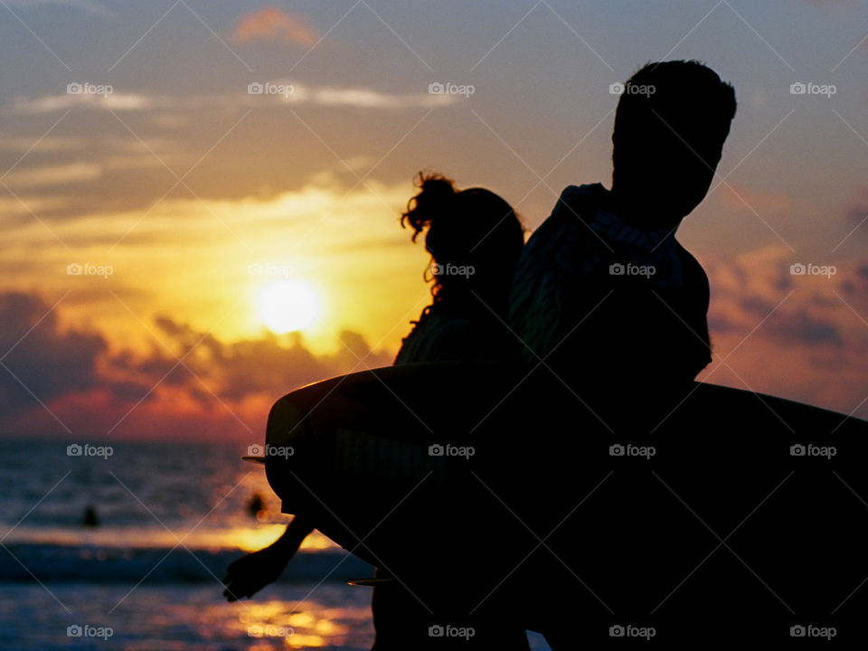 Two surfers walking along the beach at sunset in silhouette. 