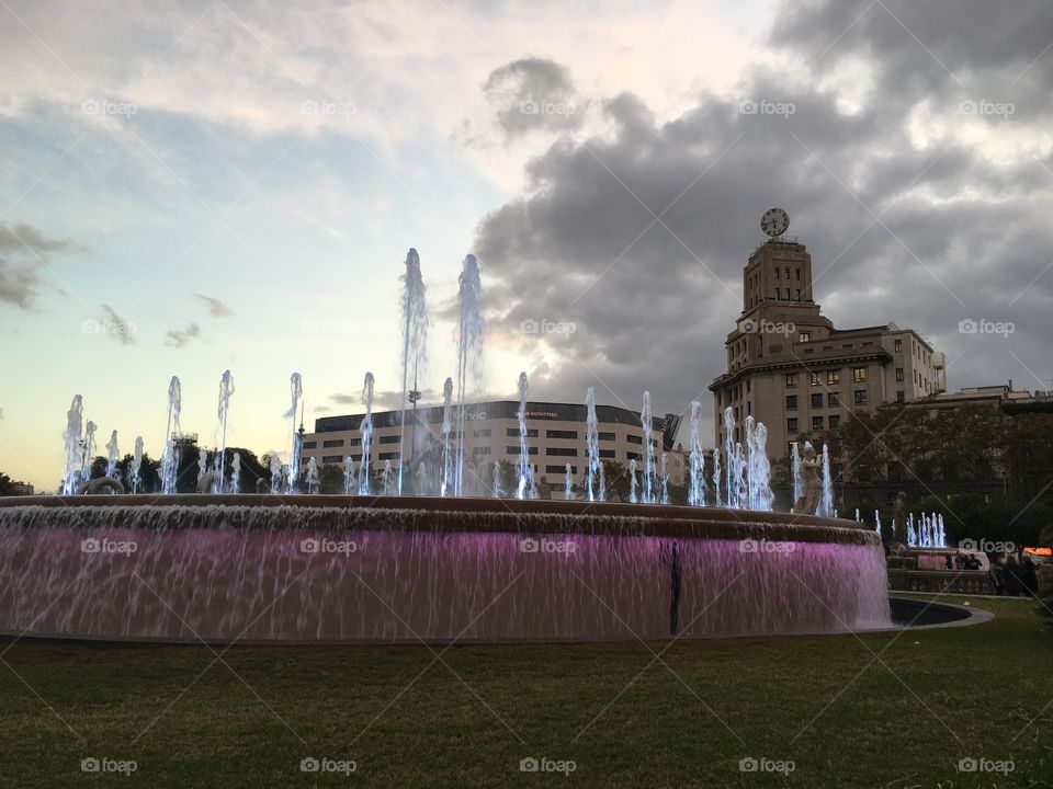 One of the two round fountains lit up in Plaça de Catalunya at night.