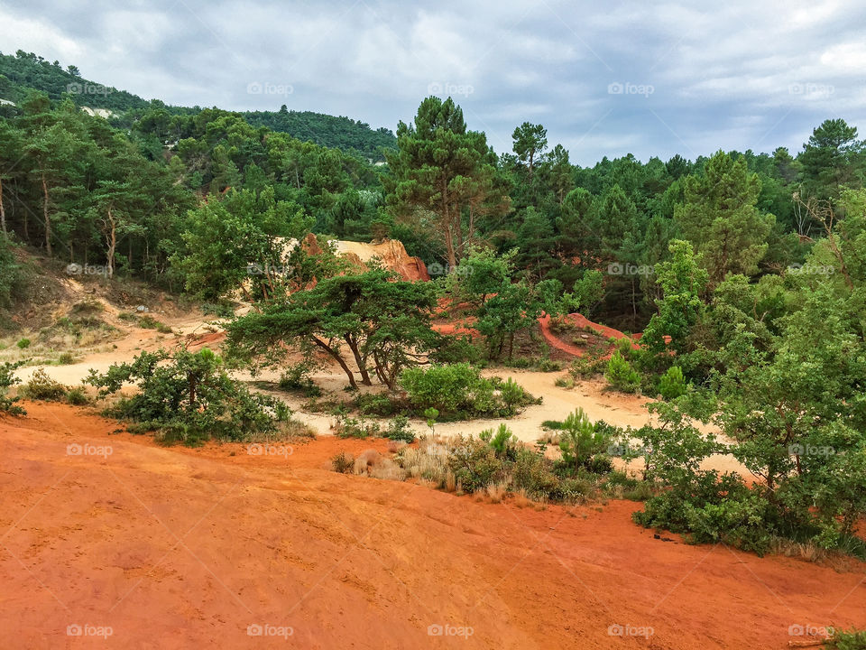 Nature reserve called Colorado Provencal in France with trees and orange colored sand dunes high as mountains a rainy day in summer.