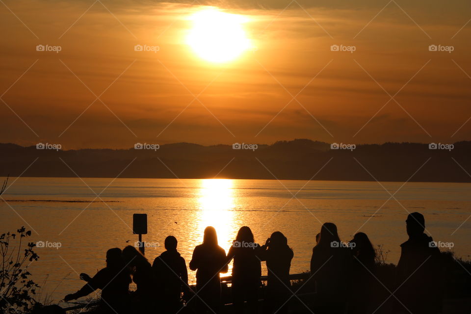 Bunch of friends watching the sunset by the shore, capturing it with smartphones , making selfies , having a good time...