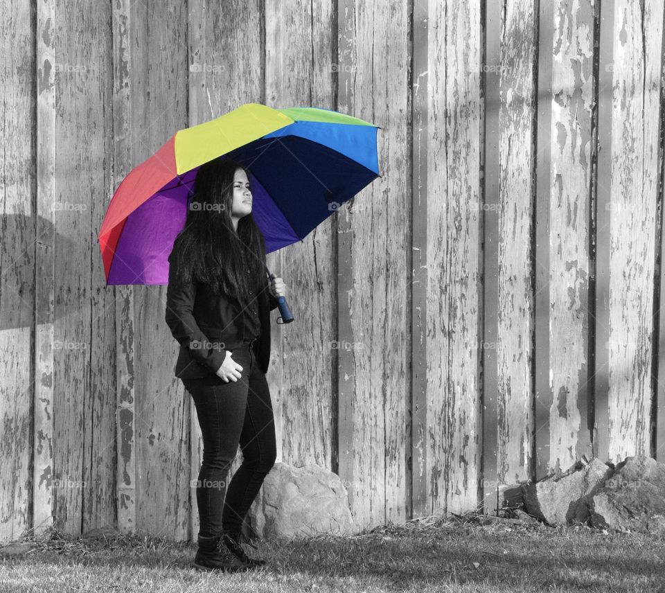Girl with rainbow colored umbrella in front of a barn, photo black and white