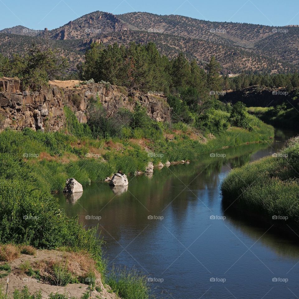 The beautiful Crooked River winds lazily through the rugged Central Oregon countryside towards the hills in the background on a sunny summer morning. 