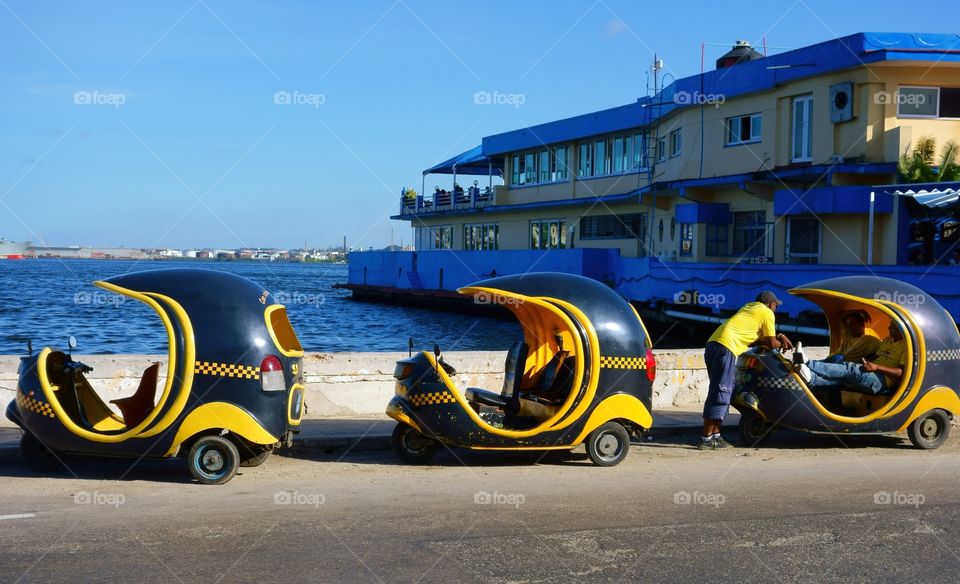 Three tricycle Taxis (Cocotaxi) and their unidentified drivers by walls of Havana harbor in Havana, Cuba on 26 December 2013.