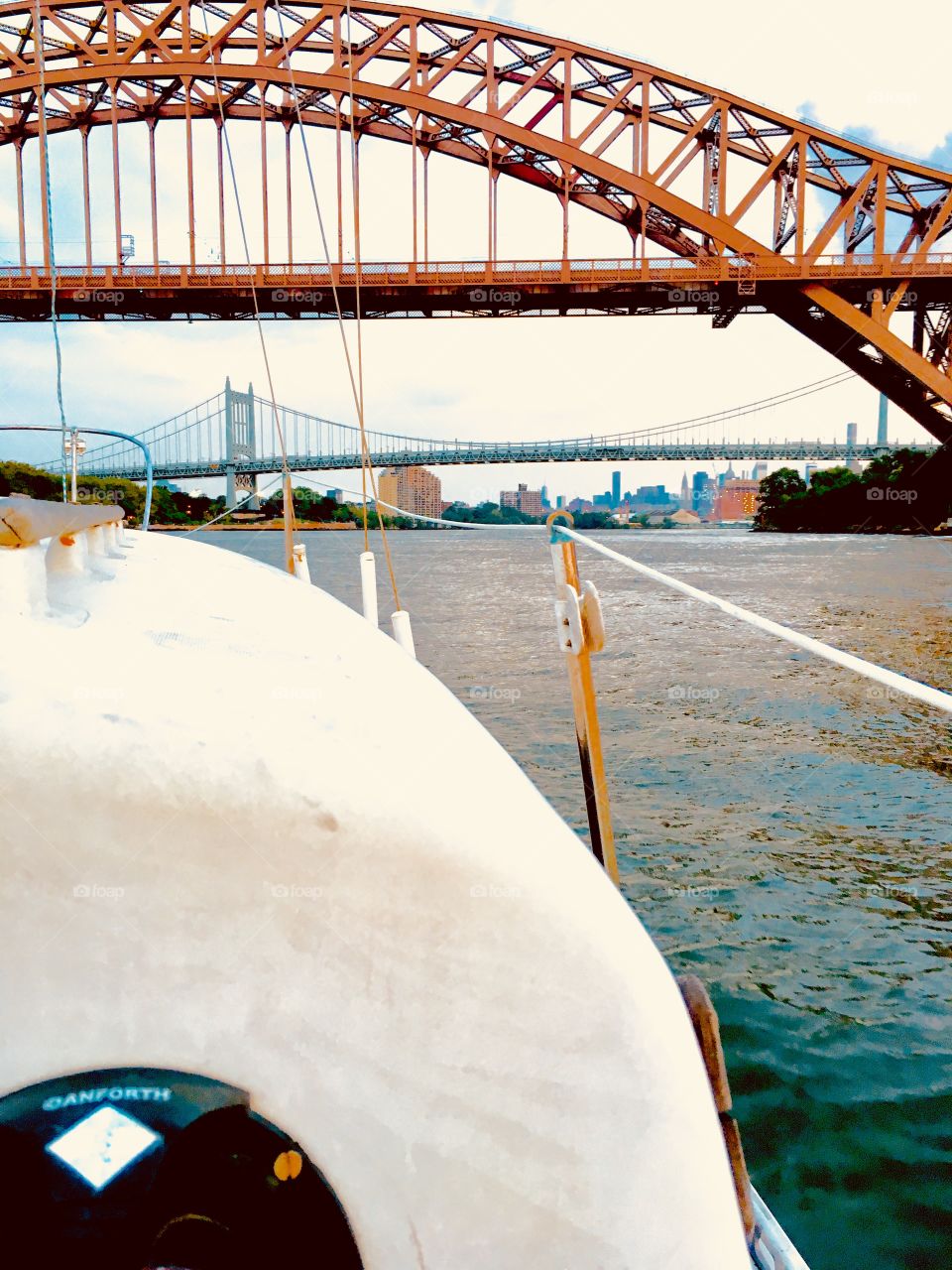The arched structures of the deck of our sailboat interspaced with the metal arch of a bridge in upper NY connecting Queens and Manhattan as seen on a southbound journey to LIC, Queens. Afar there’s yet another bridge. 2017. Hypnotic Productions