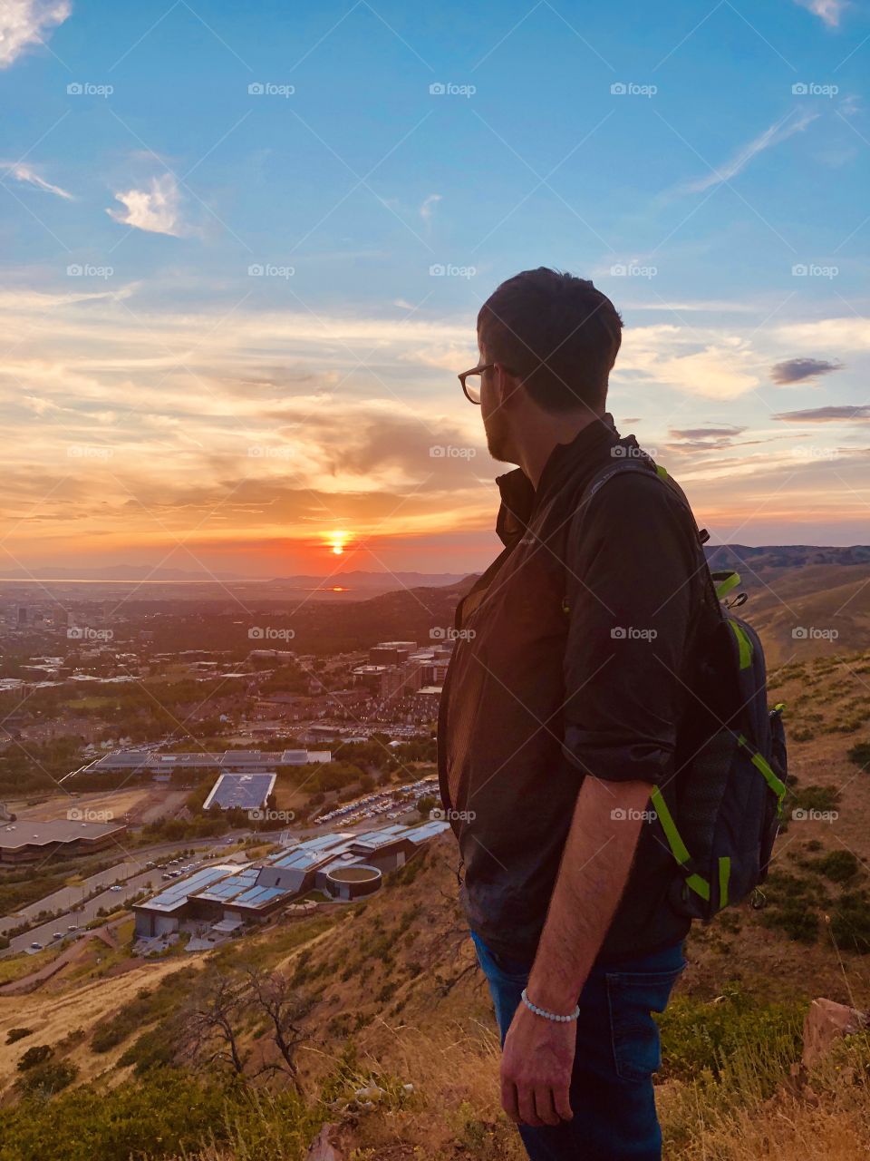 Man staring at the beautiful, orange sunset from a mountain top. The sky is colorful and calming.